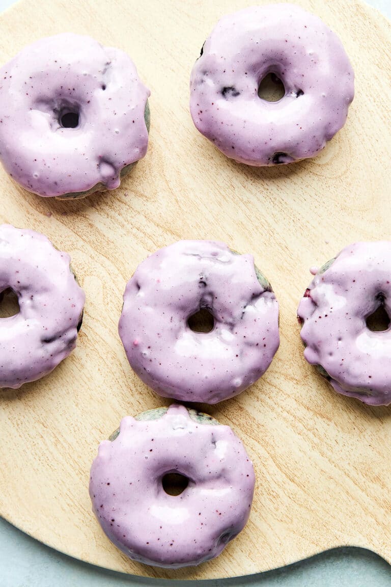 A wooden board with six wild blueberry cake donuts on top