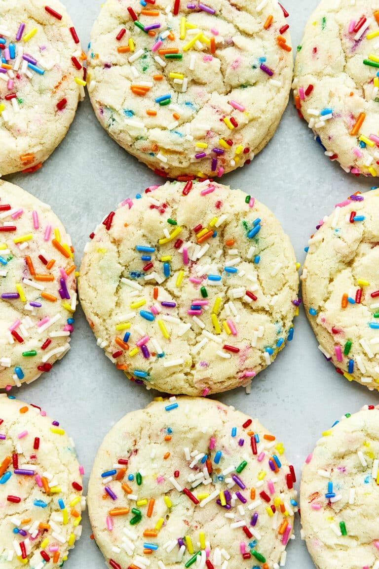 Rainbow sprinkles cookies lined up on a light blueish green surface.