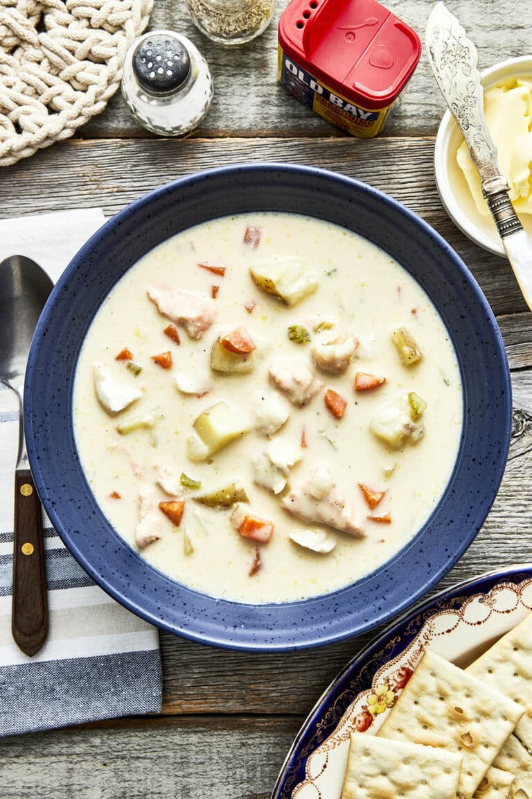 A bowl of Maritime fish chowder on a table with salt and pepper, butter, and saltine crackers.